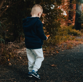 A small white boy in khakis and a black sweatshirt walks along a asphalt path