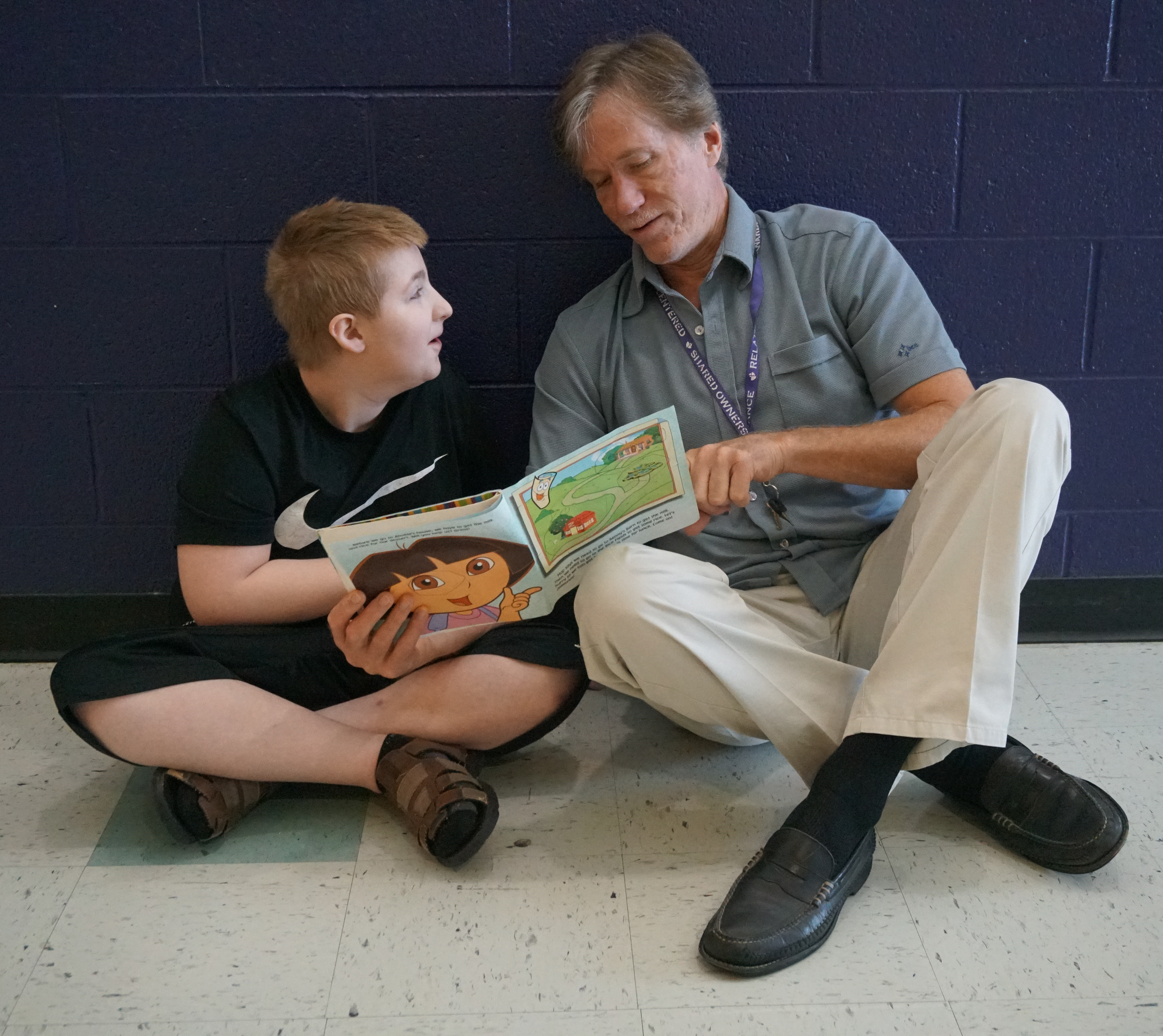 David sits on the floor and reads a book with a student