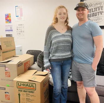 Savanah and David stand beside U-Haul brand boxes in an office area