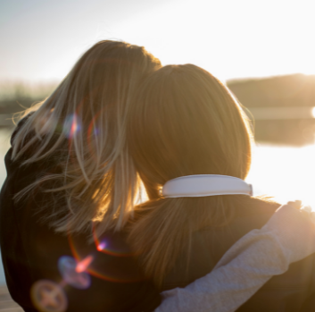 Two women embrace and look out at a sunset together