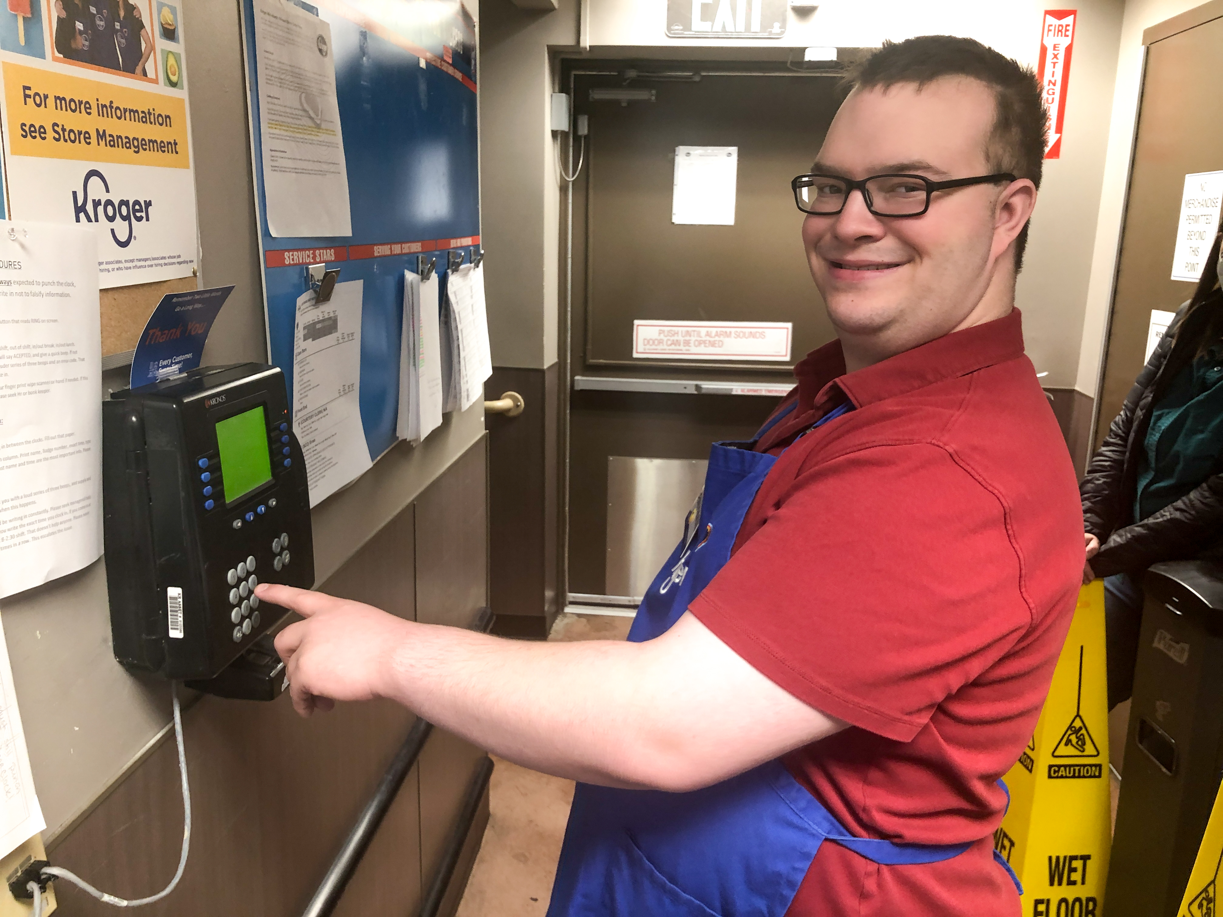 Ben smiles at the camera while he punches out on the work clock