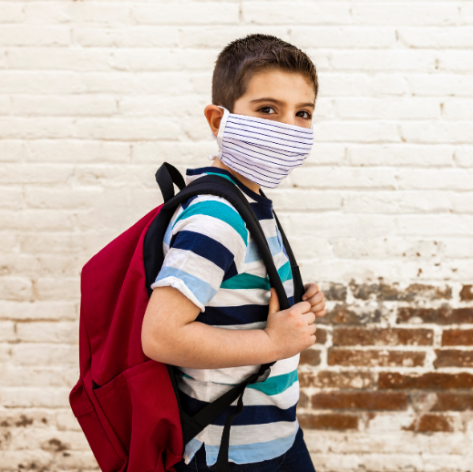 Student wearing mask and red backpack standing in front of brick wall