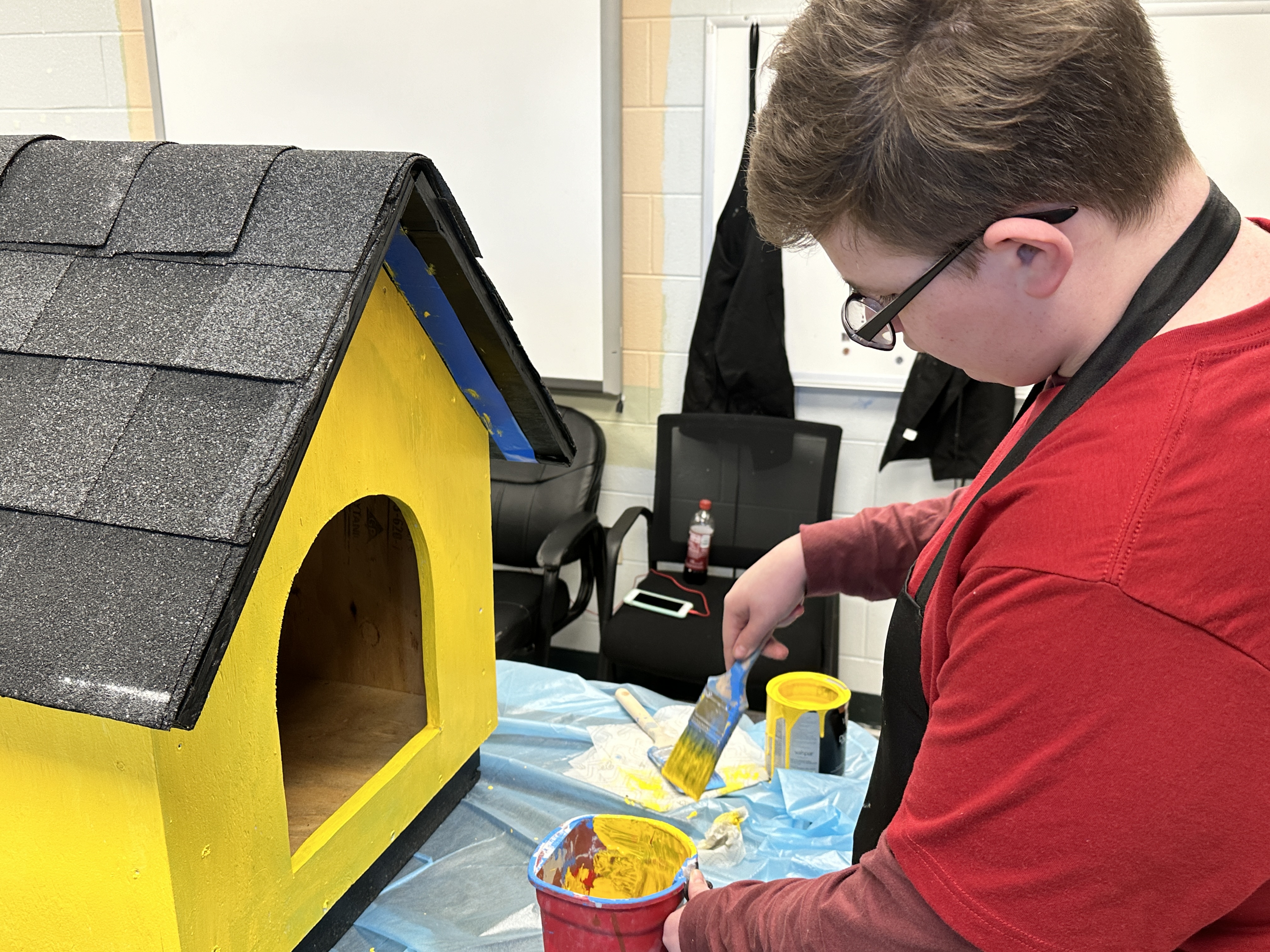 A boy paints a dog house bright yellow