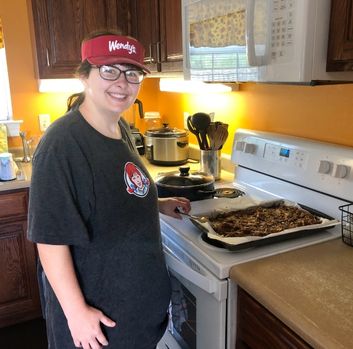 Margaret Maxie stands in her kitchen smiling at the camera with her Wendy's hat and shirt on