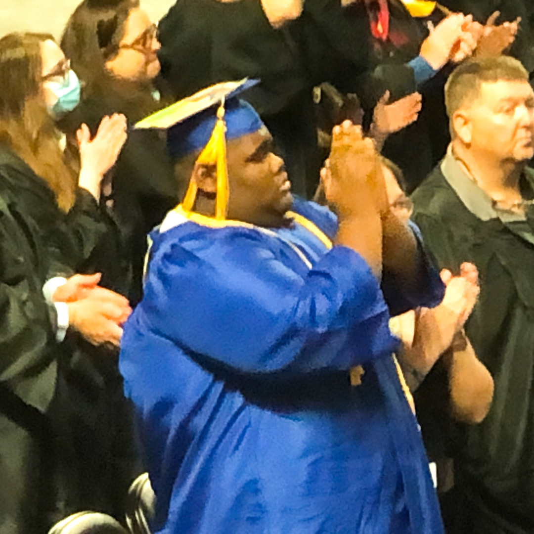 Urias wearing his blue graduation cap and gown claps during graduation