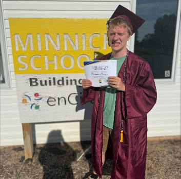 A student stands in a graduation gown next to a Minnick Schools sign
