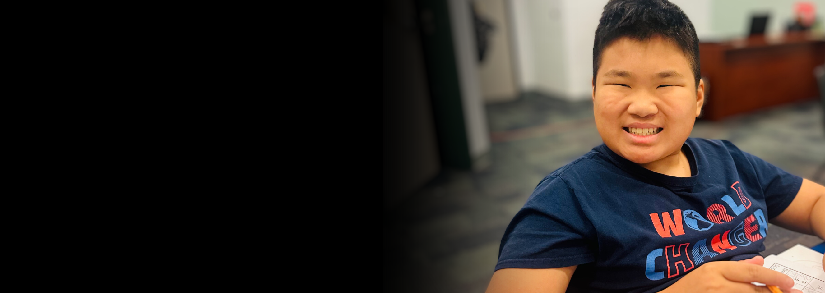 An Asian boy sits at a desk and smiles at the camera