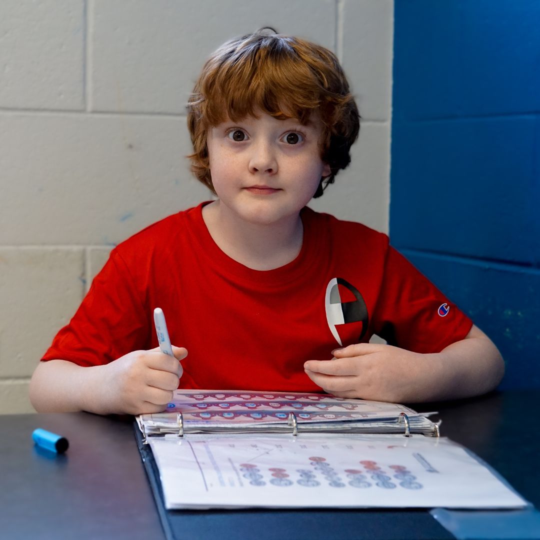 A young white student with shaggy red hair and big, brown eyes wearing a red shirt looks at the camera