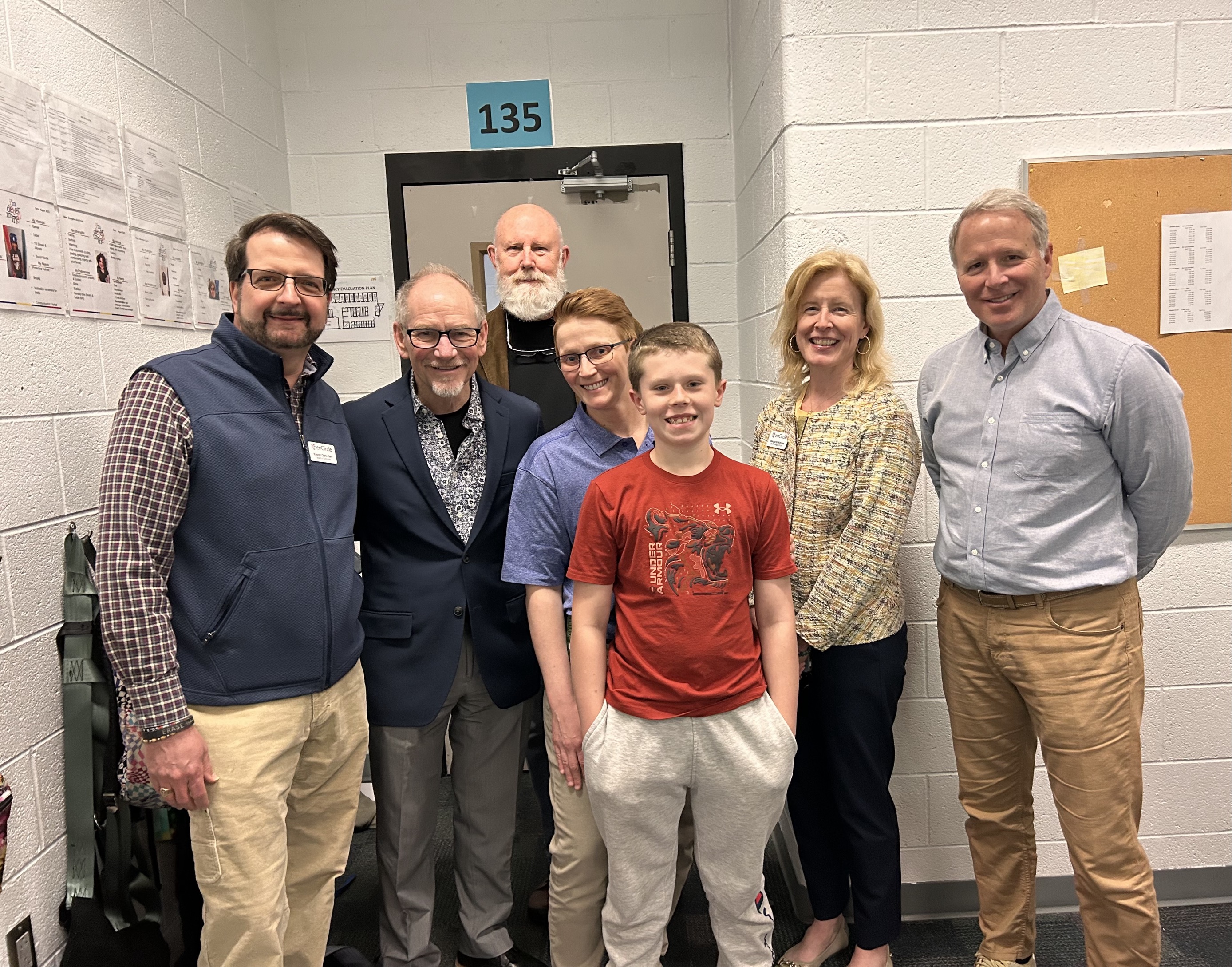Staff stand smiling with a student in and classroom