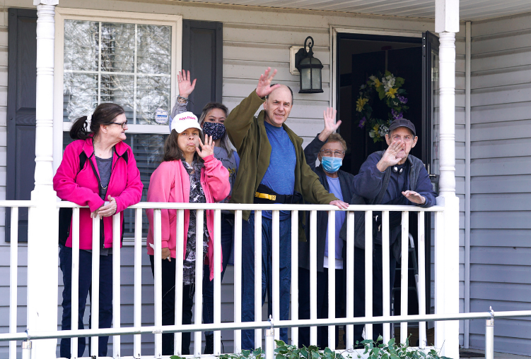 Six people stand on a porch and wave at the camera