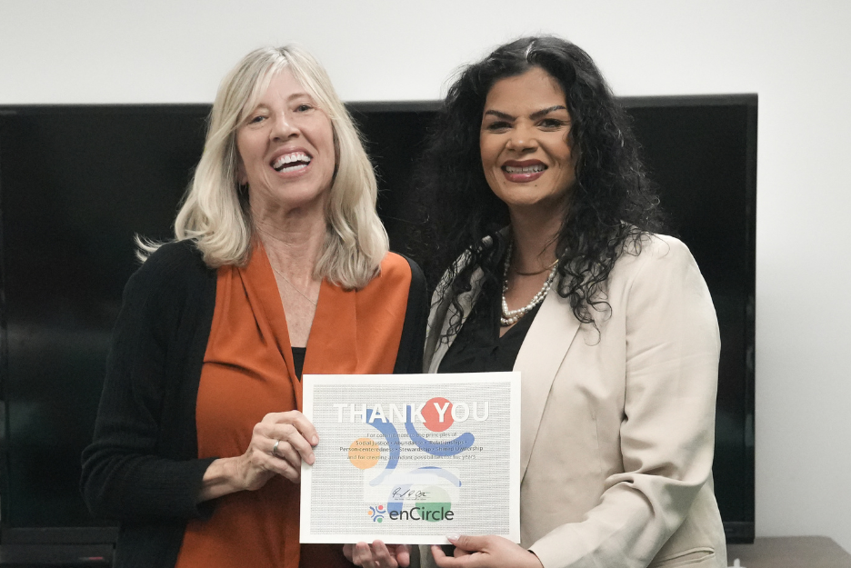 Two staff members smile and hold up a certificate that says 